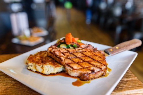 Grilled steak with a crosshatch pattern, served with a side of mashed potatoes and fresh vegetable garnish.