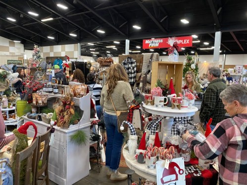 A bustling indoor market with vendors and shoppers, featuring holiday decorations and various crafts for sale.