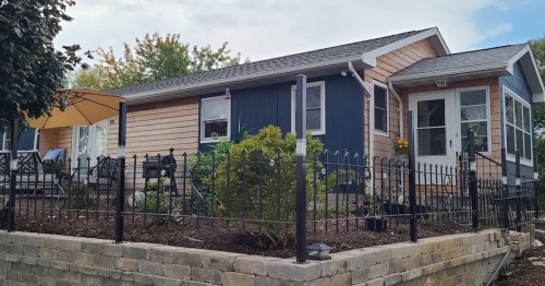 A cozy house with a blue and wood exterior, surrounded by a black fence and landscaped garden.