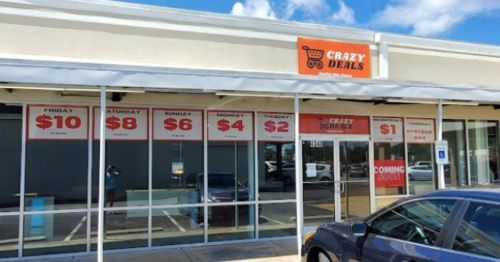 Storefront of "Crazy Deals" with promotional signs displaying daily discount prices. Clear blue sky in the background.