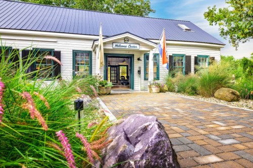 A welcoming center with a landscaped pathway, featuring a stone entrance and flags, surrounded by greenery.