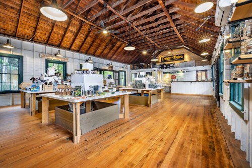 Interior of a rustic shop with wooden beams, tables displaying products, and large windows letting in natural light.