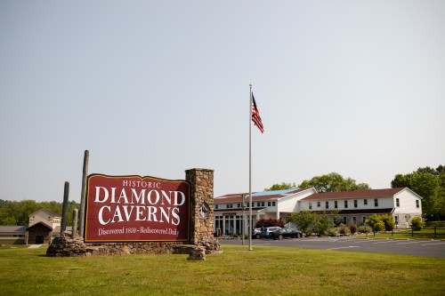 Sign for Historic Diamond Caverns with an American flag and a building in the background on a clear day.