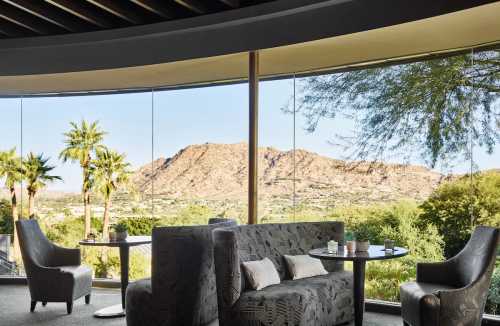 A modern lounge with large windows showcasing a mountain view and palm trees outside.