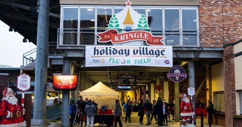 Entrance to Kringle Holiday Village at Fluor Field, featuring festive decorations and visitors gathering outside.