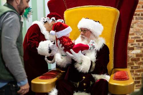 Santa and Mrs. Claus hold a festive stocking while sitting on a large, decorated throne.