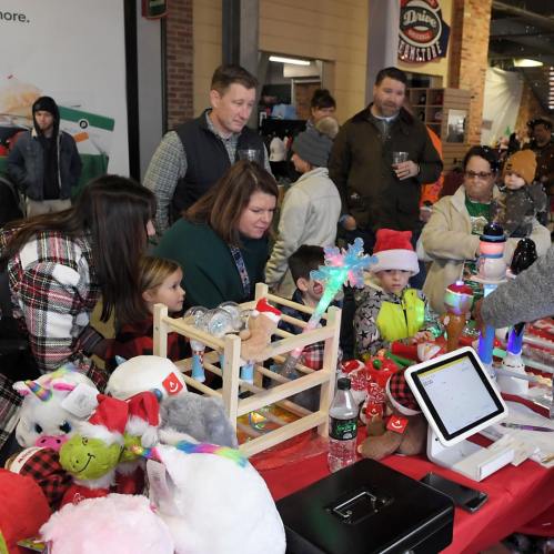 A busy holiday market scene with families exploring toys and decorations at a festive table.