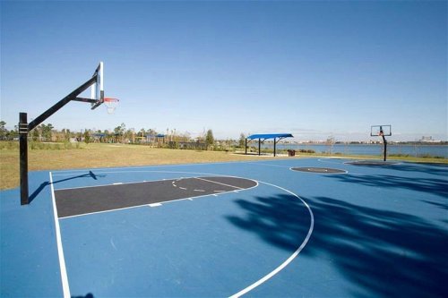 A blue outdoor basketball court with two hoops, surrounded by grass and a view of a lake in the background.