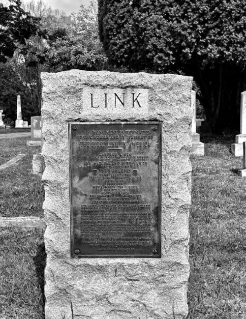 A stone monument in a cemetery with the name "LINK" at the top and an engraved plaque detailing memorial information.