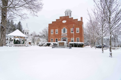 A brick building with a dome, surrounded by snow-covered trees and a gazebo, under a clear winter sky.