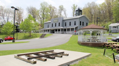 A gray building with a bell tower, surrounded by greenery, a gazebo, and a red car parked nearby.
