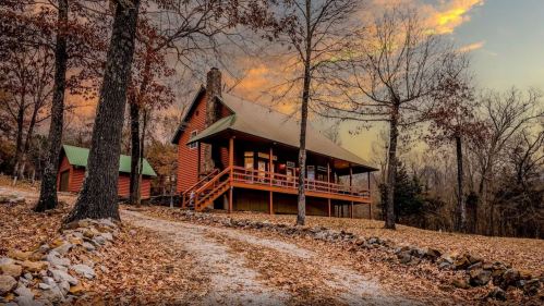 A rustic cabin surrounded by autumn leaves and trees, with a gravel path leading to its porch at sunset.