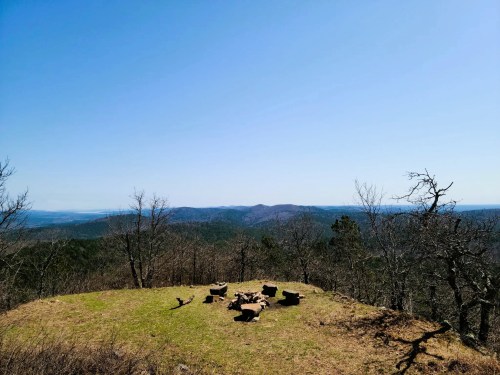 A scenic view of rolling hills under a clear blue sky, with a grassy area and scattered logs in the foreground.