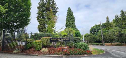 Entrance to Lake View Cemetery, featuring a sign, greenery, and a cloudy sky.