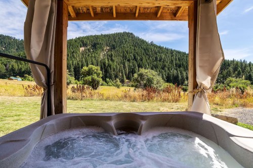 A hot tub with bubbling water, framed by a wooden structure, overlooking a lush green mountain landscape.