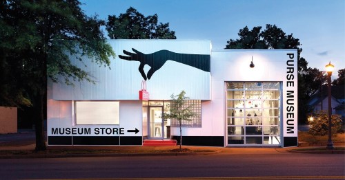 Exterior of the Purse Museum at dusk, featuring a large hand silhouette and a sign for the museum store.