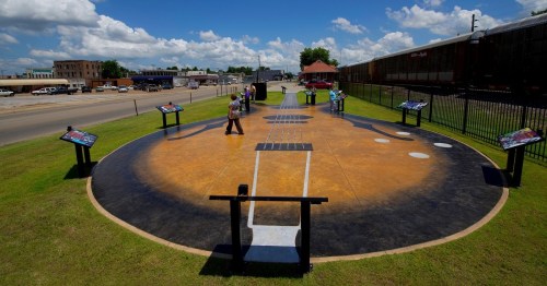 A large guitar mural on the ground with people walking around, surrounded by informational signs and a blue sky.