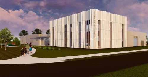 Modern building with a sleek design, surrounded by greenery, featuring people walking towards the entrance.