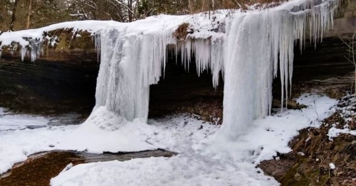 A frozen waterfall surrounded by snow-covered rocks and trees, creating a serene winter landscape.