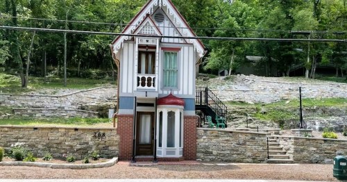 A charming, two-story house with a unique design, surrounded by greenery and stone landscaping.