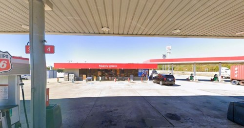 A gas station with a red roof, featuring pumps and a convenience store, under a clear blue sky.