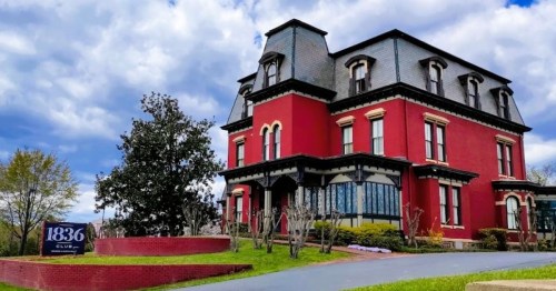 A large red Victorian-style house with a steep roof, surrounded by greenery and a sign reading "1836 Club."