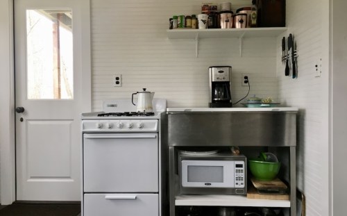 A modern kitchen with a white stove, stainless steel counter, microwave, and shelves filled with kitchenware.