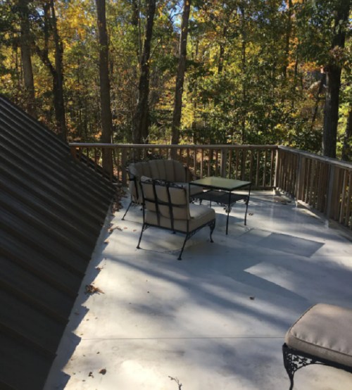 A serene outdoor deck with metal furniture, surrounded by trees and autumn foliage.