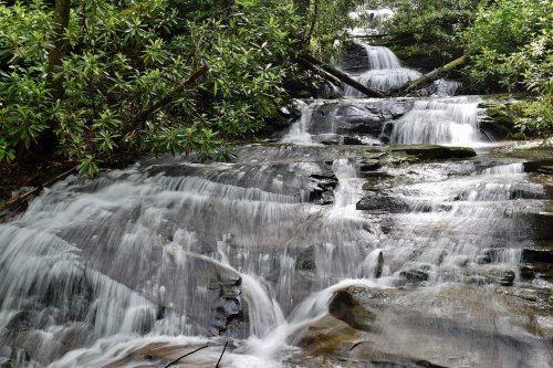 A serene waterfall cascading over rocks, surrounded by lush green foliage in a tranquil forest setting.
