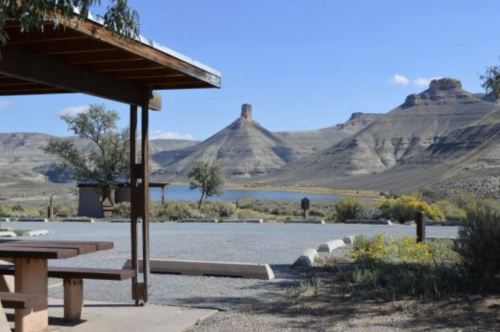 A scenic view of a desert landscape with a picnic area, mountains, and a lake under a clear blue sky.