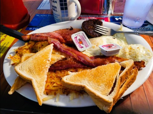 A hearty breakfast plate with eggs, bacon, sausage, hash browns, and toast, served with butter and jam.