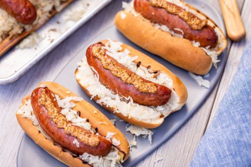 Three hot dogs in buns topped with sauerkraut and mustard, served on a gray plate.