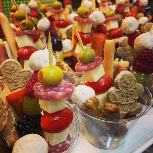 Colorful skewers of cheese, meats, olives, and fruits arranged in cups, featuring festive gingerbread cookies.