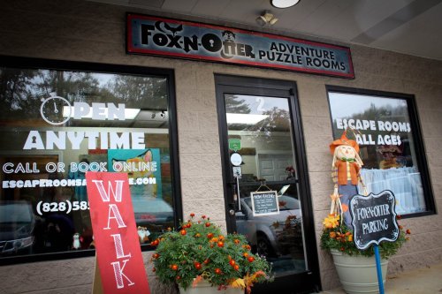 Exterior of Fox N' Otter Adventure Puzzle Rooms, featuring a sign, flowers, and a welcoming entrance.