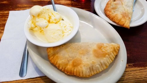 A plate with a golden-brown empanada and a bowl of vanilla ice cream on the side.