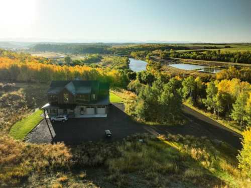 Aerial view of a modern house surrounded by trees and a winding river, with mountains in the background.