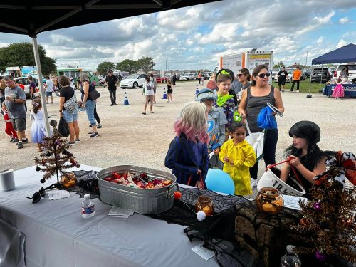 A festive outdoor event with children in costumes, a decorated table, and families enjoying the atmosphere.