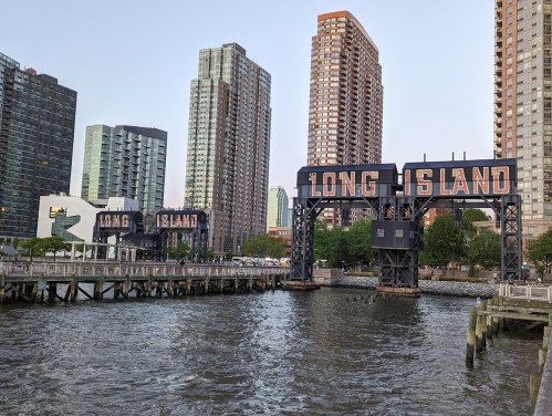 View of the Long Island sign over the water, with modern buildings in the background and a clear sky.