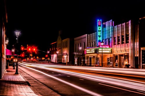 A vibrant night scene of a theater with neon lights, showcasing light trails from passing cars on a city street.