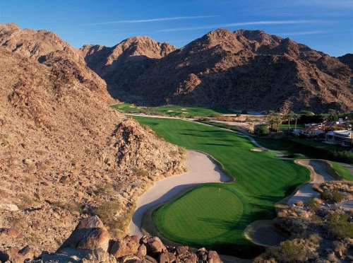 A scenic view of a golf course nestled between rocky mountains under a clear blue sky.