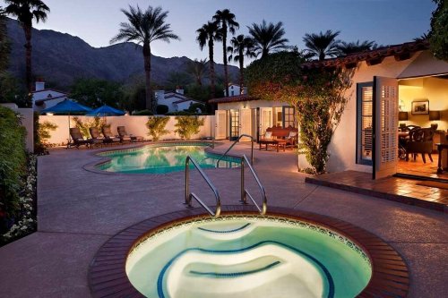 A serene pool area at dusk, featuring palm trees, lounge chairs, and a hot tub surrounded by lush greenery.