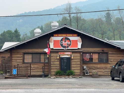 A rustic restaurant called "The Chicken Run" with a sign, additional parking, and a smoky mountain backdrop.