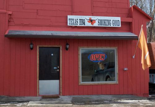 A red building with a sign reading "Texas BBQ Smoking Good" and an "OPEN" sign in the window.