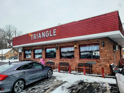 A brick building with a red roof sign reading "Triangle," surrounded by snow and parked cars.