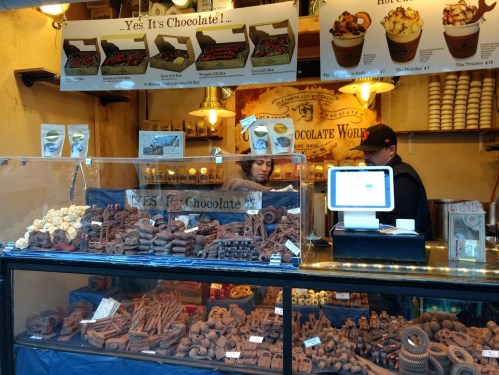 A chocolate shop display featuring various chocolate treats and desserts, with a cashier and menu overhead.