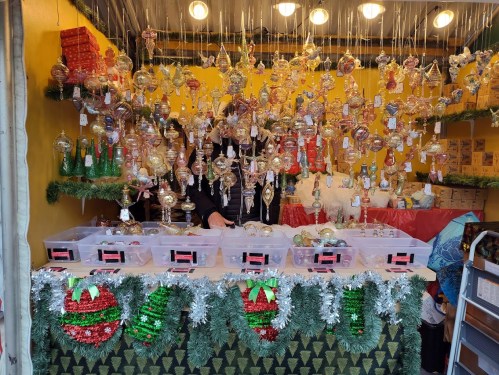 A festive market stall adorned with colorful Christmas ornaments and decorations, with bins for customers to browse.