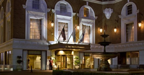The Westin Poinsett hotel entrance at night, featuring a fountain and illuminated brick facade.
