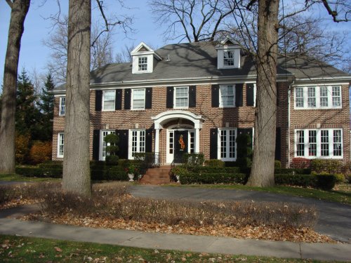 A large brick house with white trim, surrounded by trees and a neatly landscaped yard, on a quiet street.