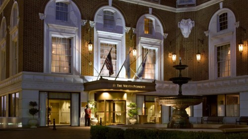 The Westin Poinsett hotel entrance at night, featuring a fountain and illuminated facade with flags.