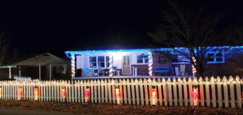 A house decorated with blue and white lights, surrounded by a white picket fence with festive lanterns.